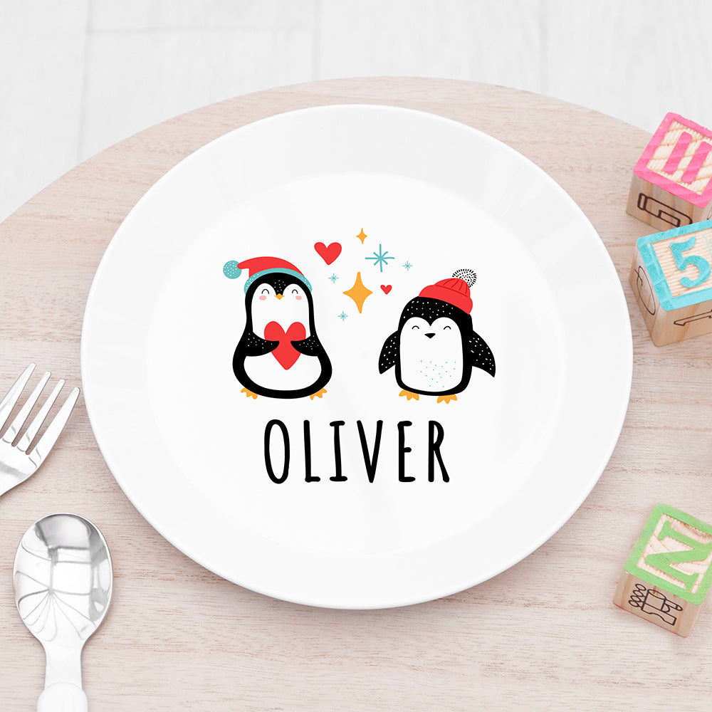 White plate with cartoon penguins and 'OLIVER' text on a wooden table.