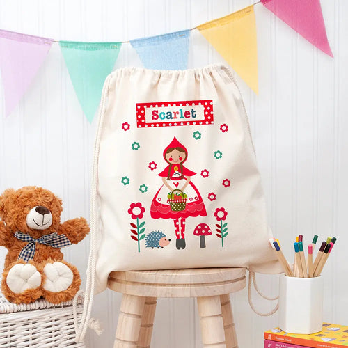 Drawstring bag with 'Scarlet' design, teddy bear, and stationery items on a wooden stool.