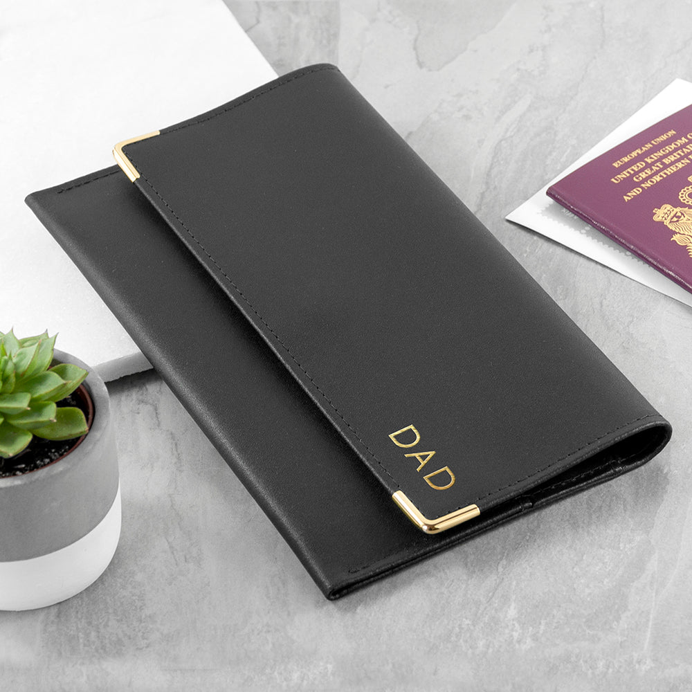 Black leather passport holder with 'DAD' engraving on a light gray surface.