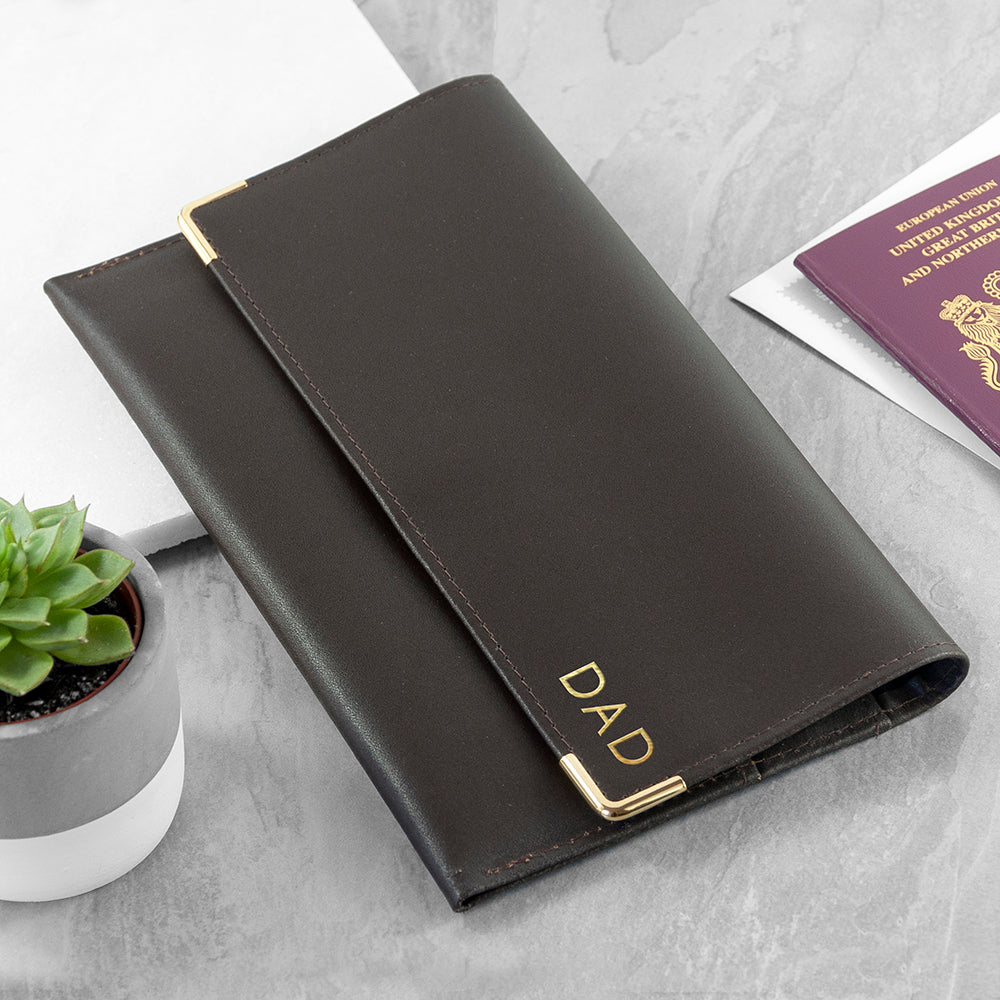 Black wallet with 'DAD' engraving on a light gray surface with a plant and passport in the background.
