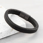Black braided bracelet with a metallic clasp on a light gray background
