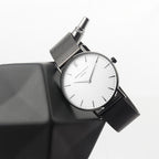 Wristwatch with silver mesh band on a reflective surface