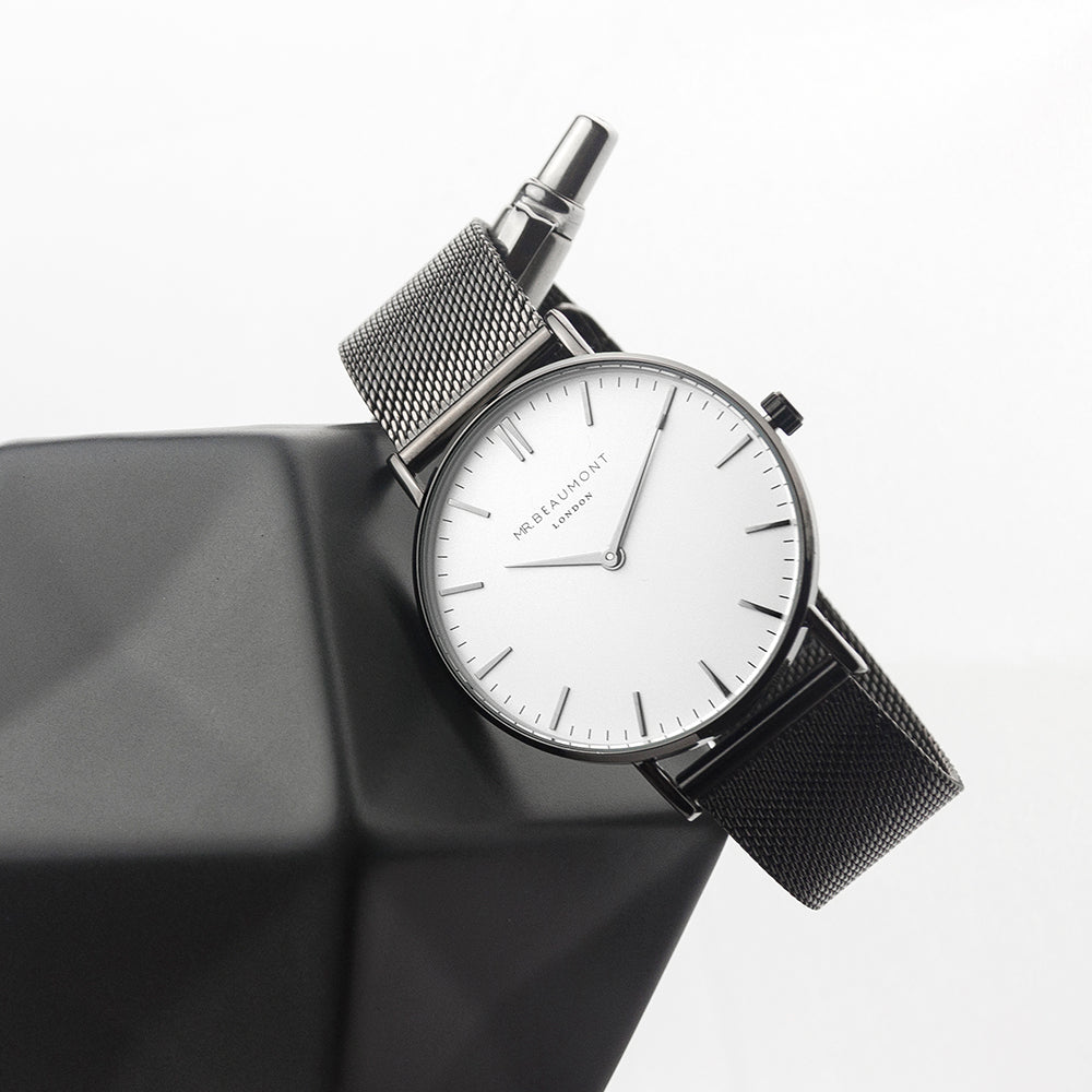 Wristwatch with silver mesh band on a reflective surface