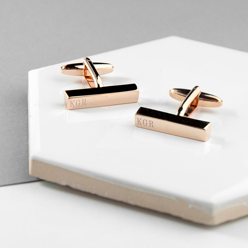 Rose gold cufflinks with 'KGR' engraving on a white surface