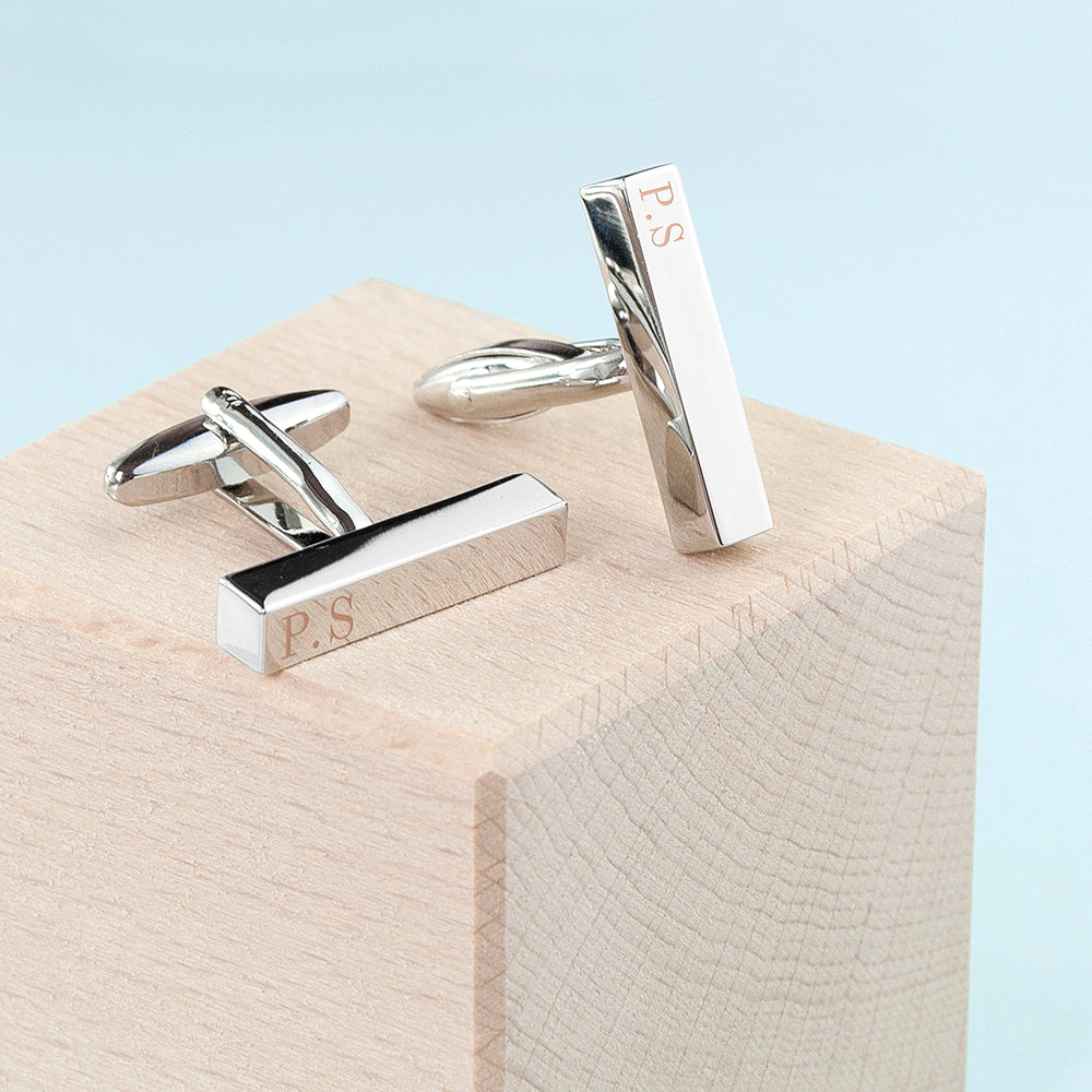 Silver cufflinks with 'P.S.' engraving on a wooden block with light blue background