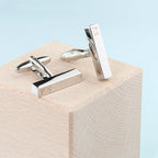Silver cufflinks with 'P.S.' engraving on a wooden block with light blue background