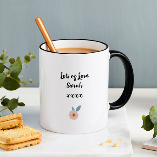 White mug with black handle and text, filled with a beverage, on a light surface with cookies and a plant.