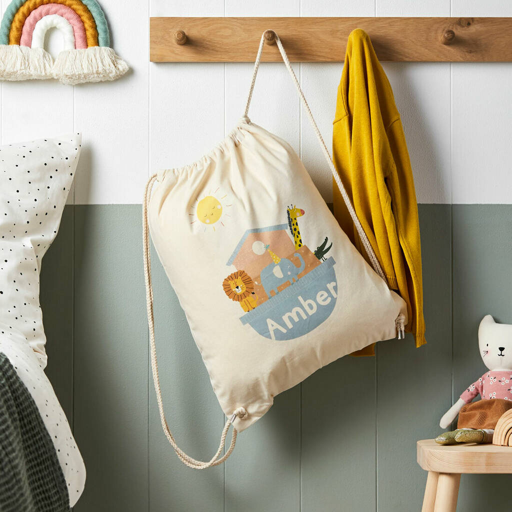 Drawstring bag with animal illustrations and 'Amber' text hanging on a wooden hook against a white wall.
