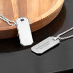 Two silver dog tags on a dark surface with a wooden object in the background
