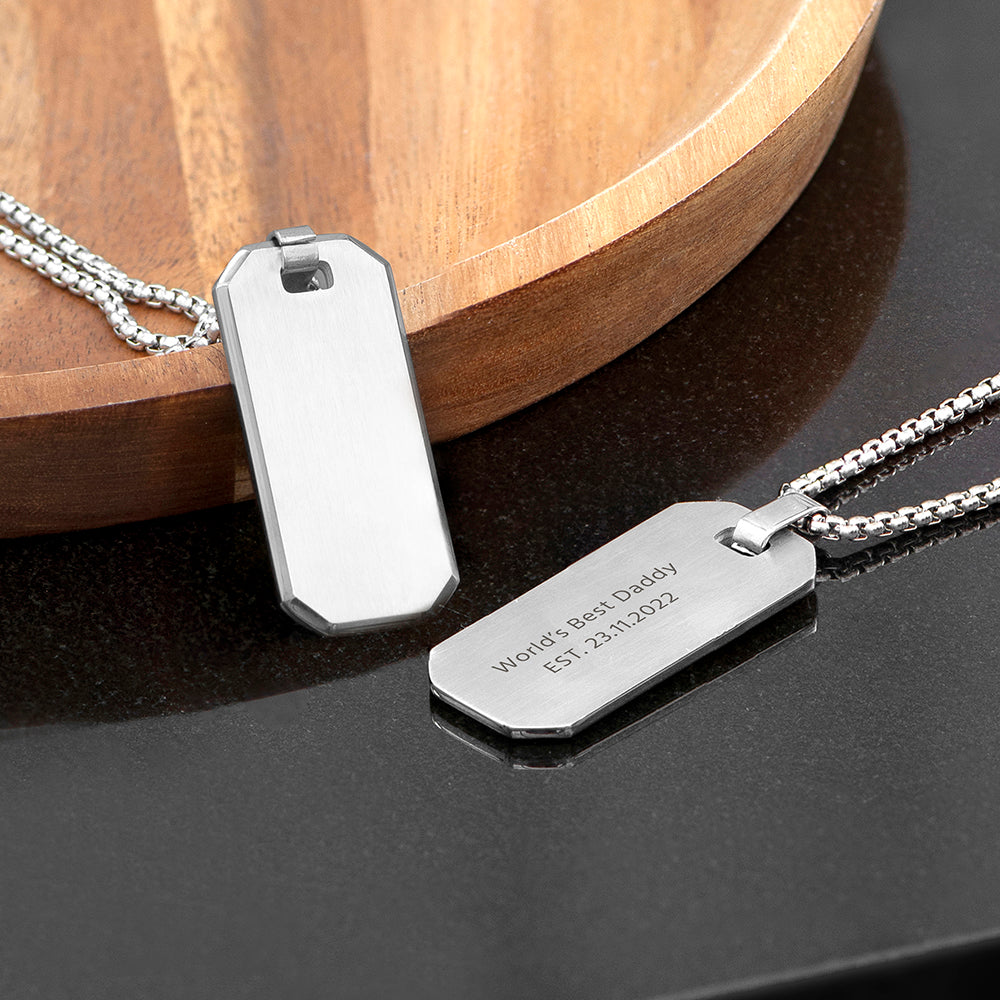 Two silver dog tags on a dark surface with a wooden object in the background