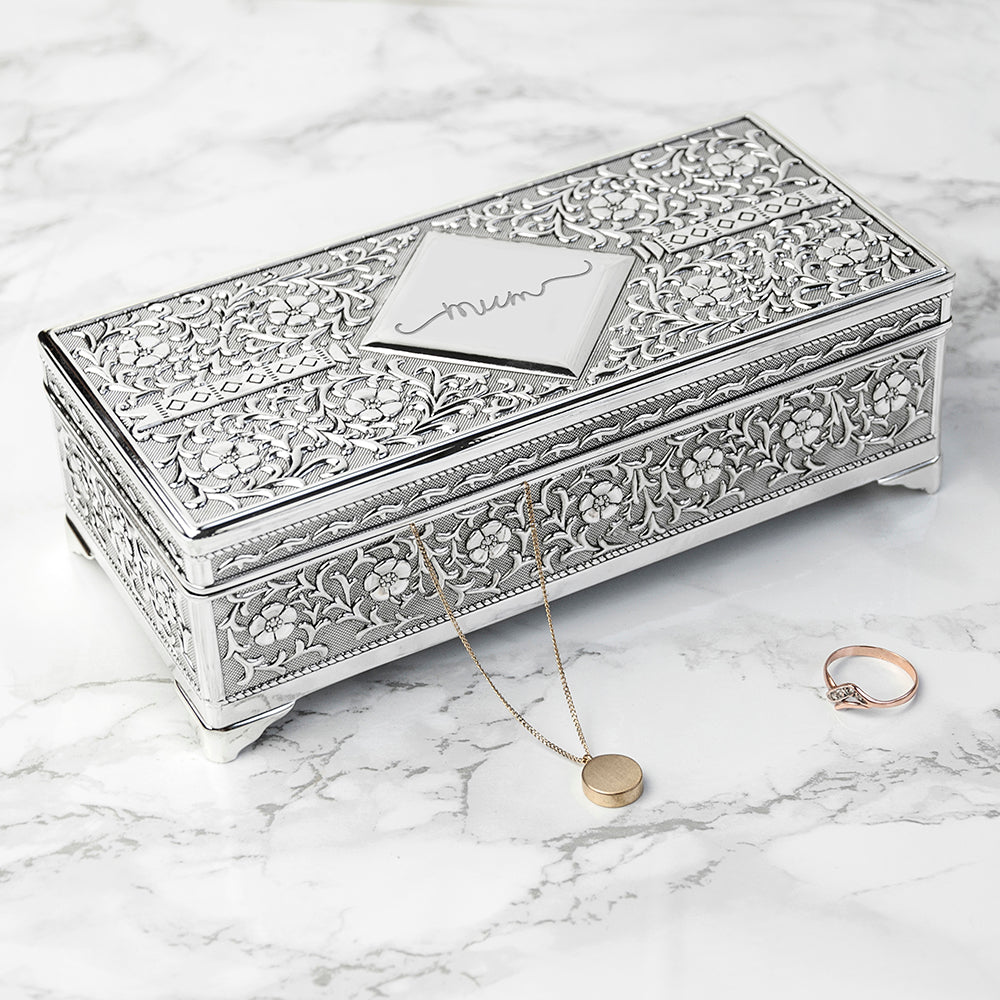 Decorative jewelry box with intricate patterns on a marble surface, accompanied by a necklace and ring.
