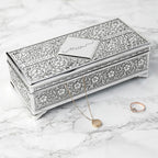 Decorative jewelry box with intricate patterns on a marble surface, accompanied by a necklace and ring.