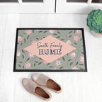 Decorative doormat with floral pattern and 'Smith Family HOME' text on a white floor with shoes and a plant.