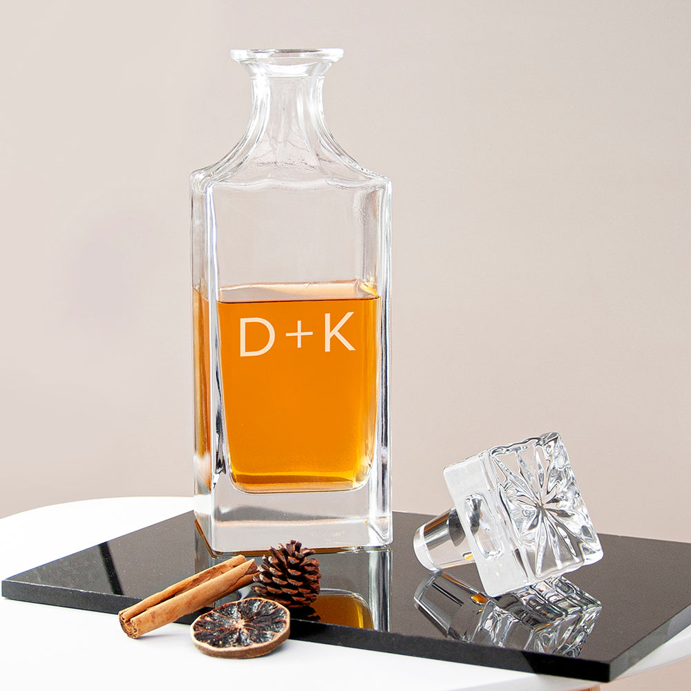 Clear glass decanter with amber liquid on a reflective surface with decorative elements.