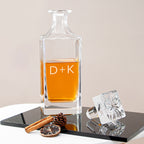 Clear glass decanter with amber liquid on a reflective surface with decorative elements.