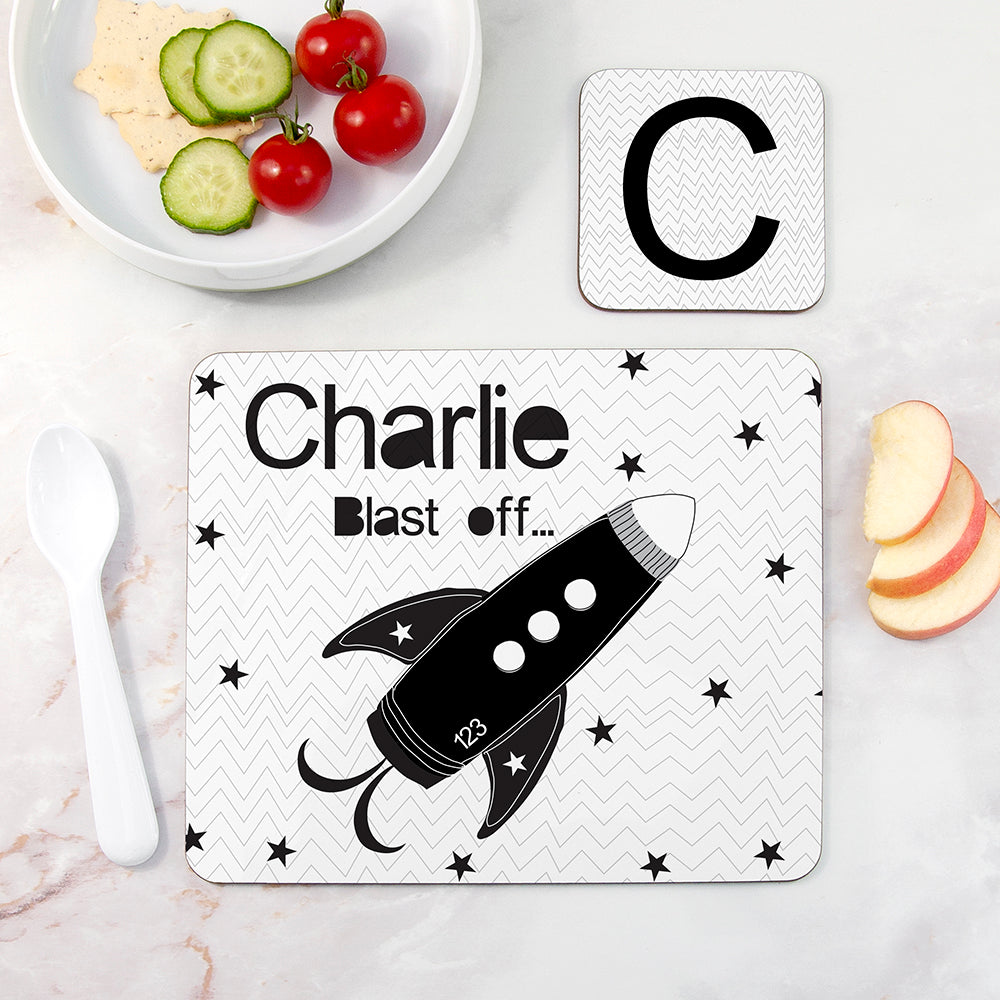 Personalized placemat with a rocket design and name 'Charlie' on a table with food.