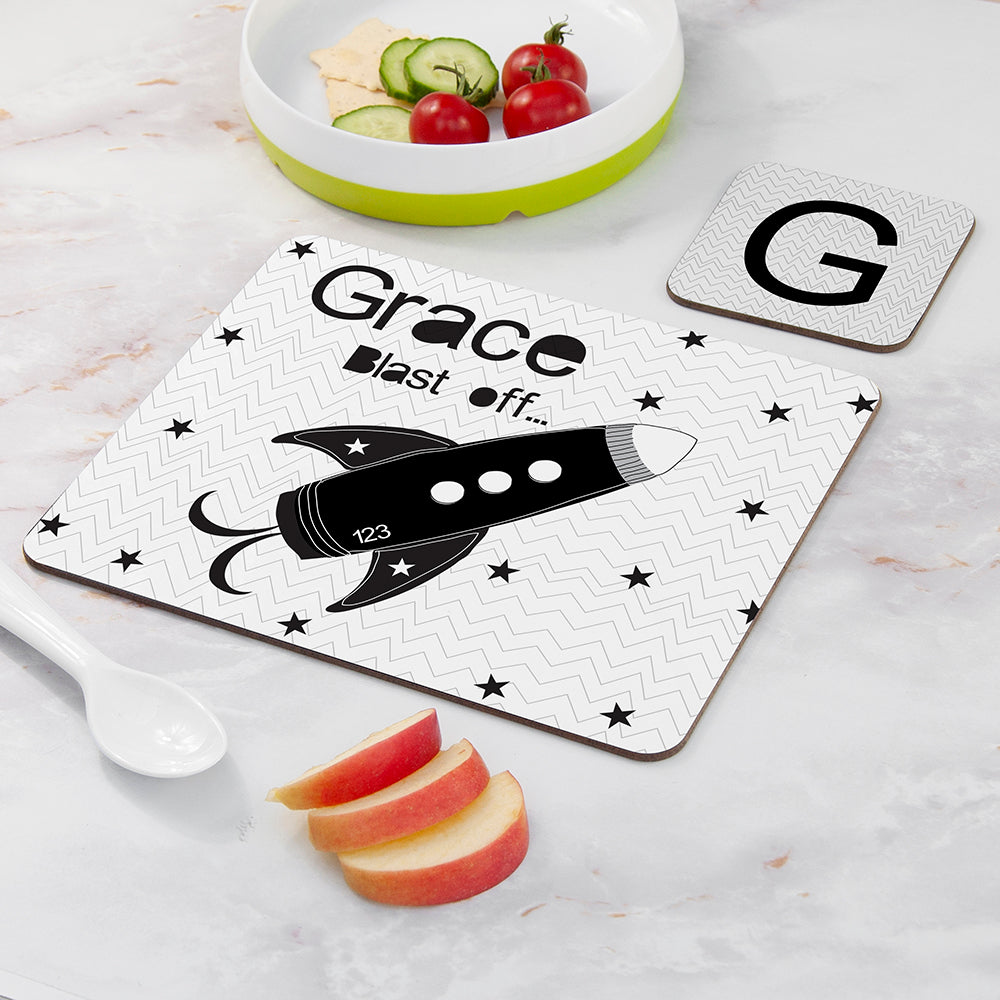 Personalized cutting board with a rocket design and text on a marble surface with apples and a bowl of vegetables.