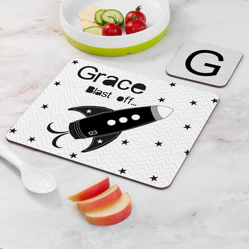 Personalized cutting board with a rocket design and text on a marble surface with apples and a bowl of vegetables.