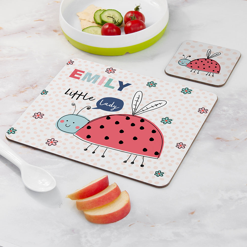 Children's placemat with ladybug design and name 'Emily' on a marble surface with fruit.