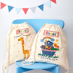 Two drawstring bags with cartoon designs and names on a blue chair with a colorful flag banner.