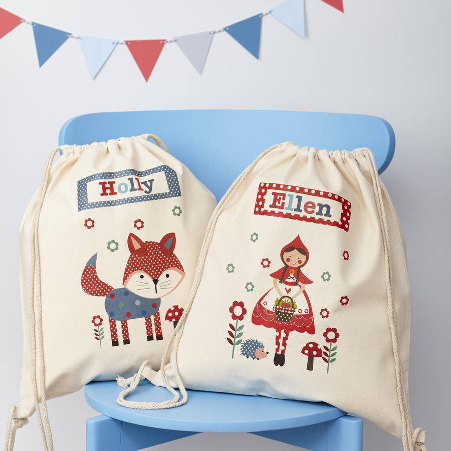 Two drawstring bags with embroidered designs of a fox and a fairy tale character on a blue chair.