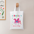White tote bag with a unicorn design and the name 'Emily' on a beige wall.