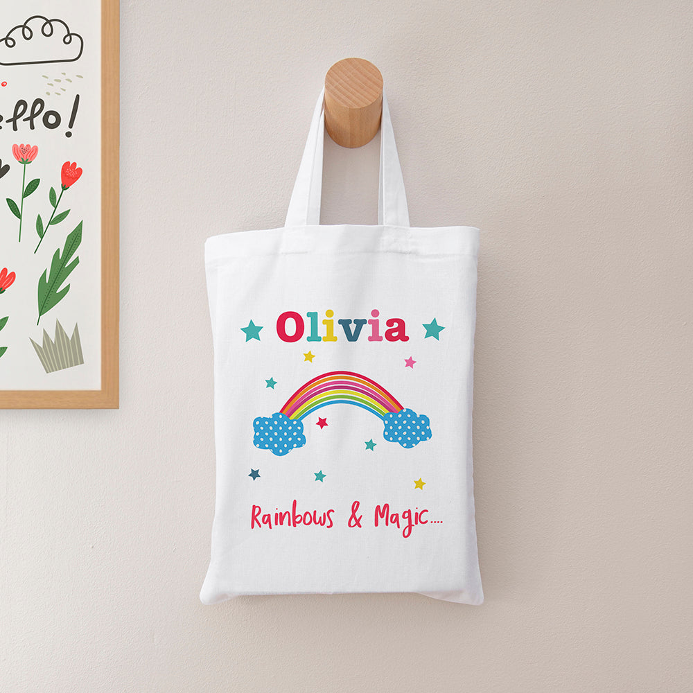 White tote bag with colorful design and text hanging on a wooden hook against a light wall.