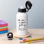 White water bottle with a cat illustration and text on a wooden surface with books and pencils.