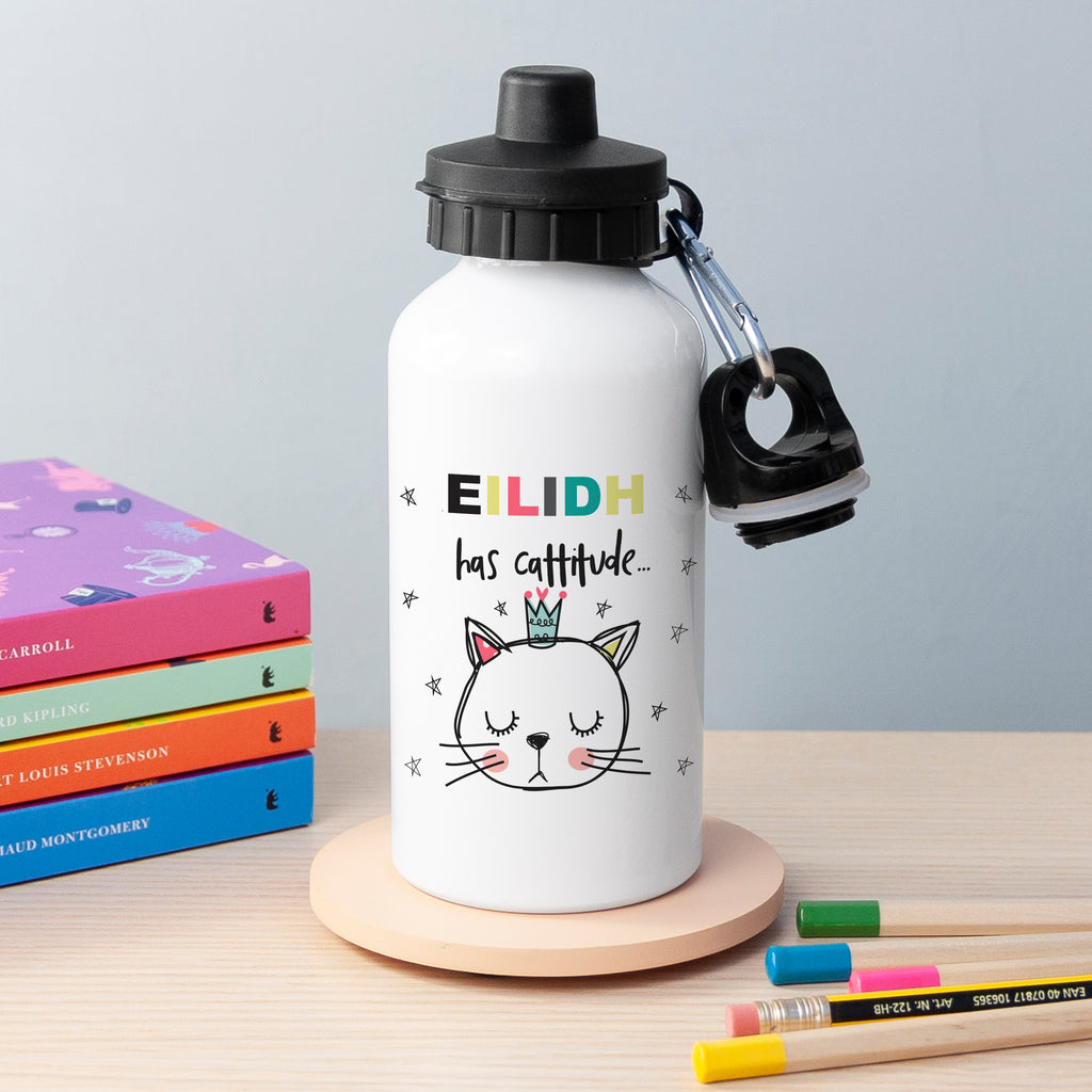 White water bottle with a cat illustration and text, placed on a wooden stand with books and pencils in the background.