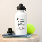 White water bottle with a cat illustration and text, placed on a wooden surface with a tennis ball and phone.