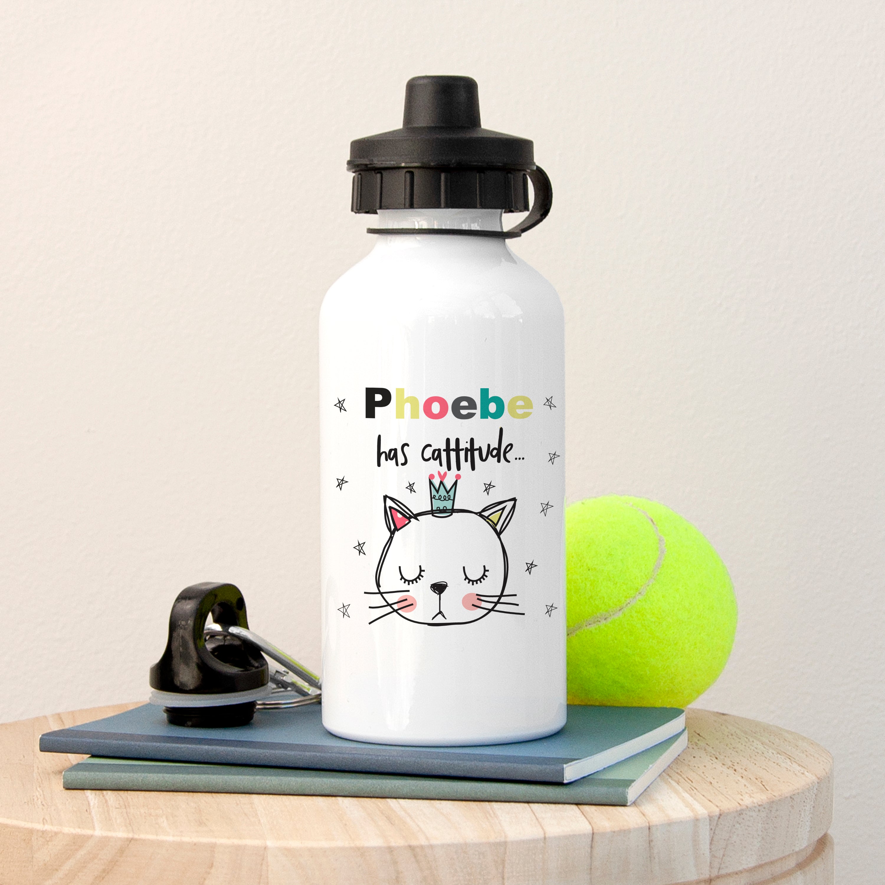 White water bottle with a cat illustration and text, placed on a wooden surface with a tennis ball and phone.