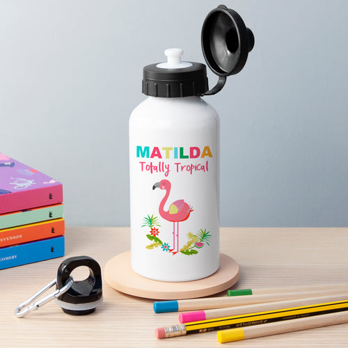 White water bottle with flamingo design and 'MATILDA Totally Tropical' text on a wooden surface with books and pencils.