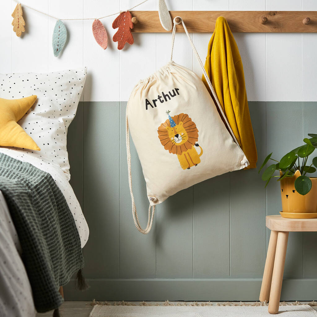 Drawstring bag with a lion design and 'Arthur' text hanging on a wooden rack in a room.