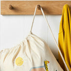 Drawstring bag with sun and giraffe design hanging on a wooden hook against a white wall.
